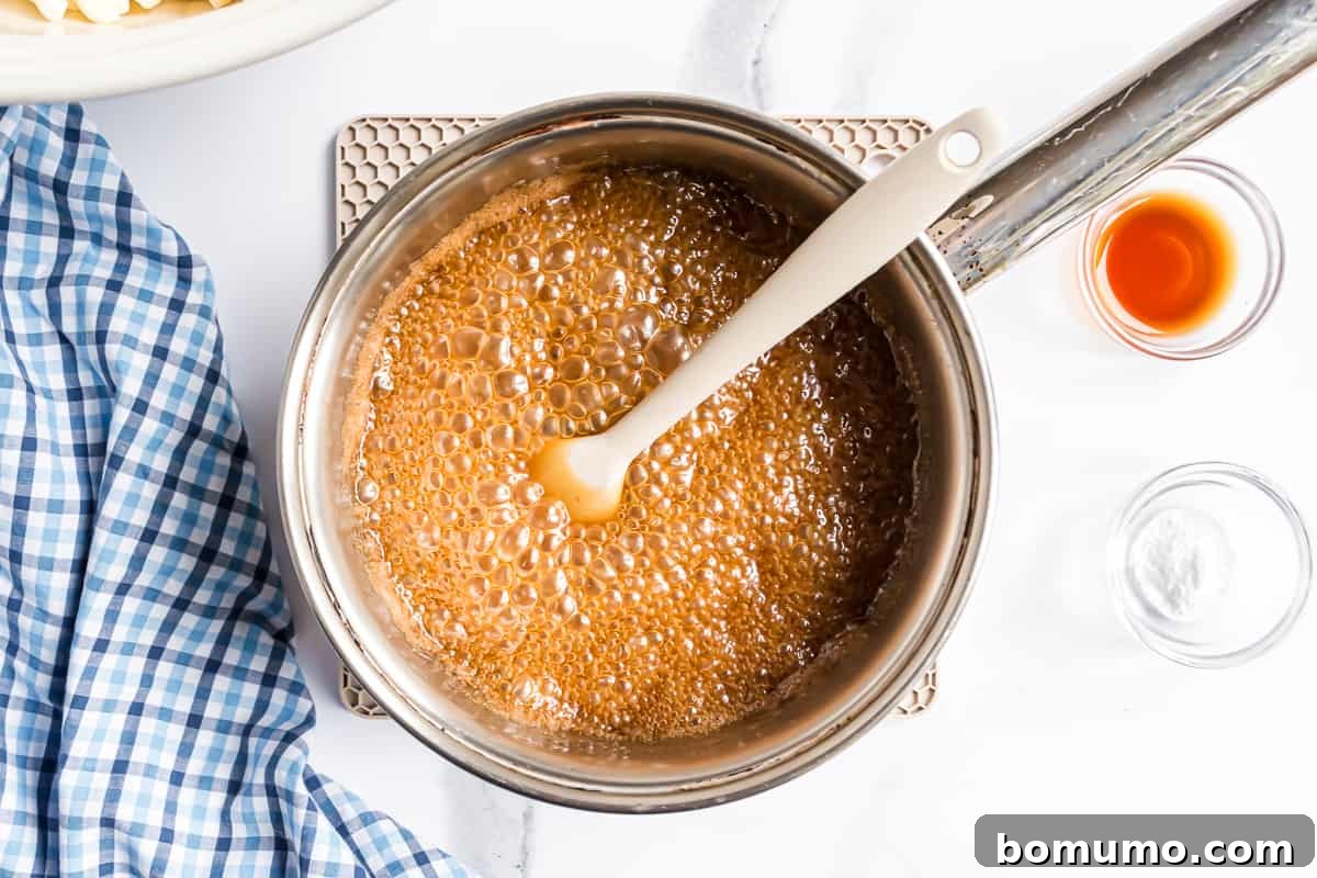 The caramel mixture bubbling gently in a saucepan, beginning to thicken and darken.