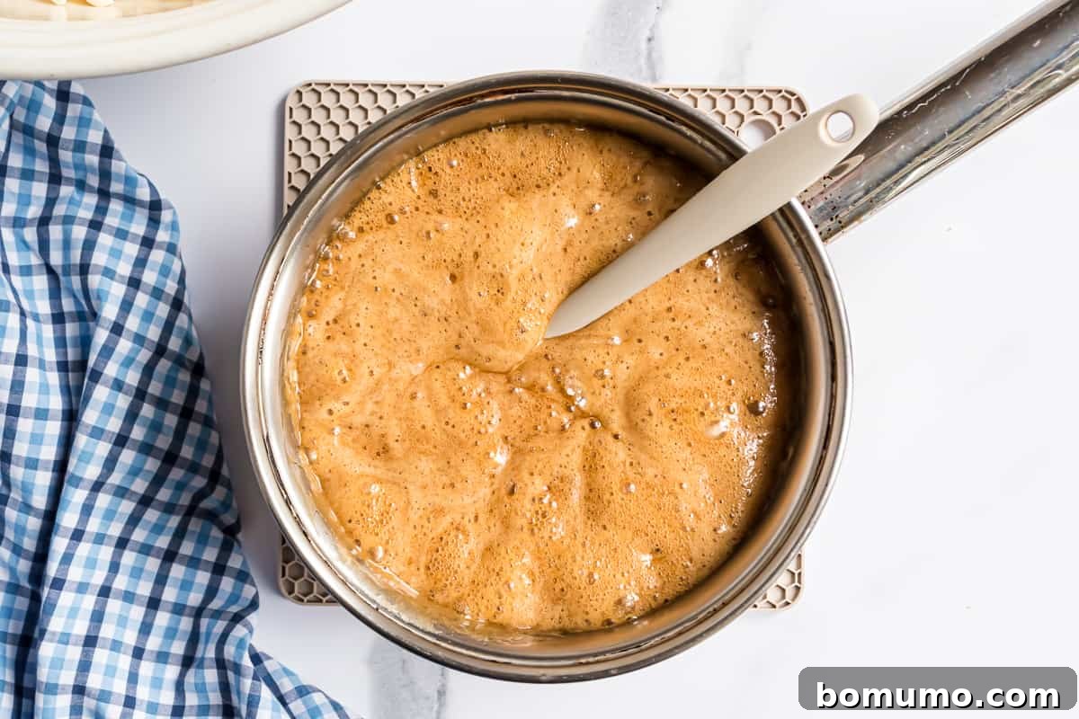 Caramel sauce foaming vigorously in a saucepan after baking soda has been added, indicating a chemical reaction.