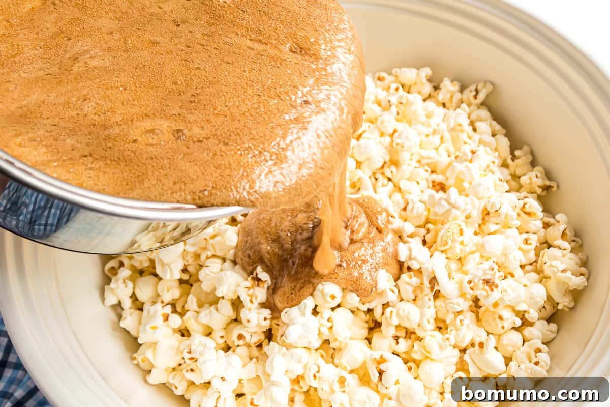 Hot, foamy caramel sauce being poured over a mound of popped popcorn in a large mixing bowl.