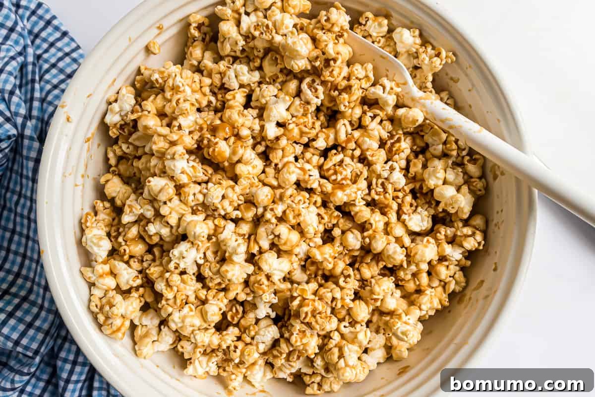 Popcorn thoroughly coated in caramel sauce, sitting in a large mixing bowl before being spread onto baking sheets.
