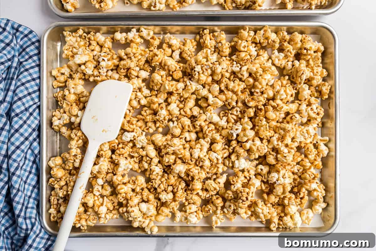 Unbaked caramel corn spread thinly and evenly onto a parchment-lined sheet pan, ready for the oven.