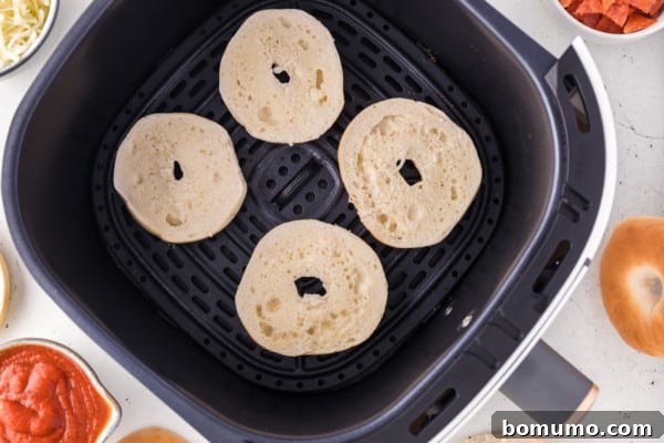 Mini bagel halves arranged in an air fryer basket, ready for toppings.
