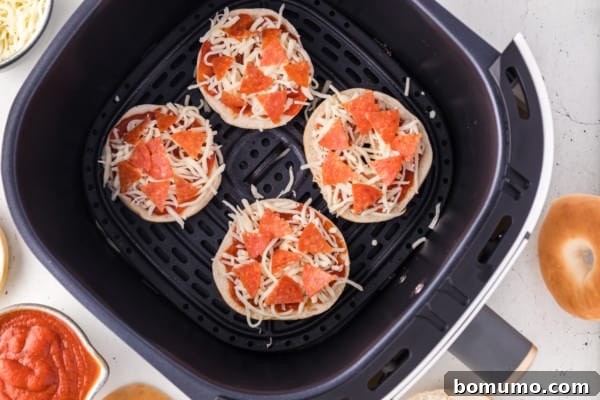 Mini bagel halves in air fryer, now complete with pizza sauce, mozzarella, and chopped pepperoni.