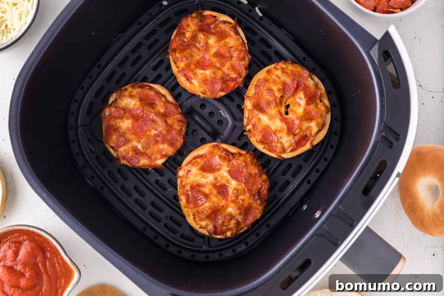 Cooked homemade bagel bites with pepperoni and cheese, golden and bubbly, in an air fryer basket.