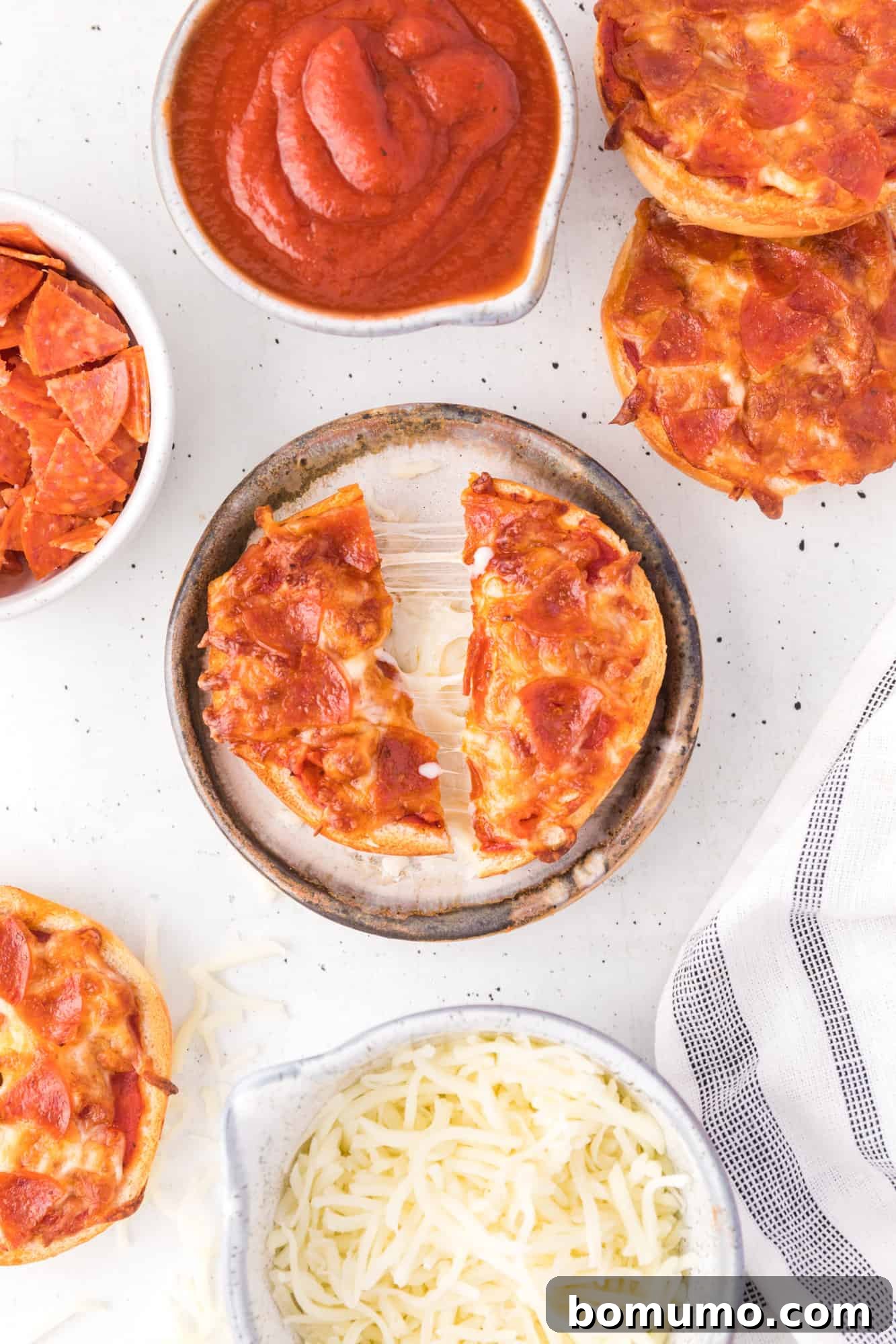 A perfectly cooked bagel bite pizza, cut in half, showcasing melted cheese and pepperoni, presented on a white plate.