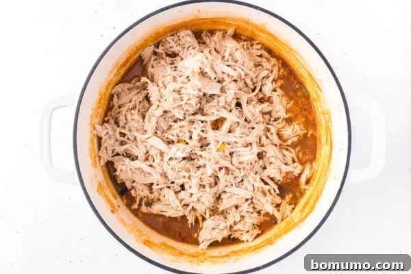 Tender shredded chicken being added back into the pot with the simmering taco soup ingredients.