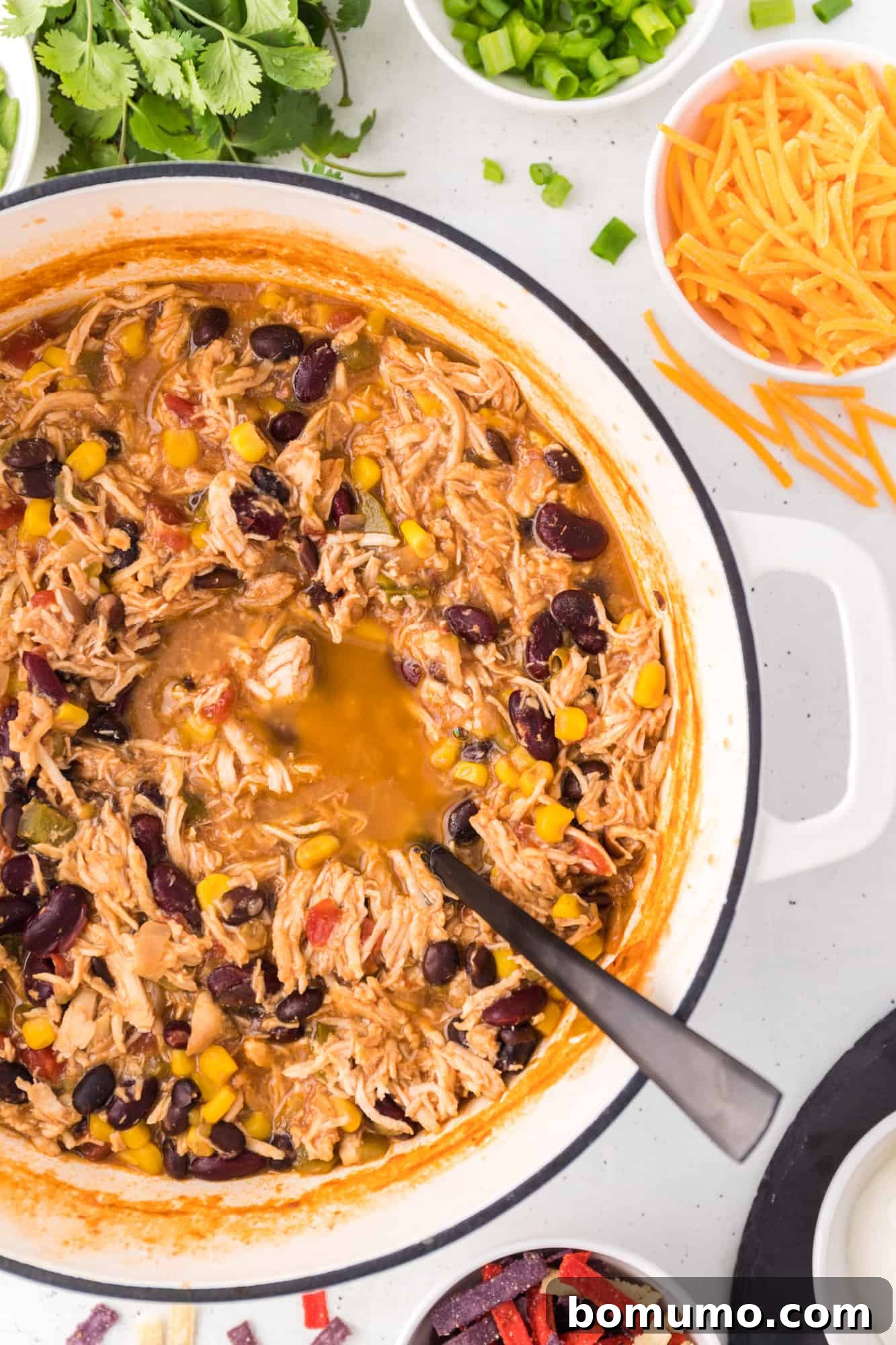 An overhead view of a large pot brimming with savory chicken taco soup, with a serving spoon resting inside.