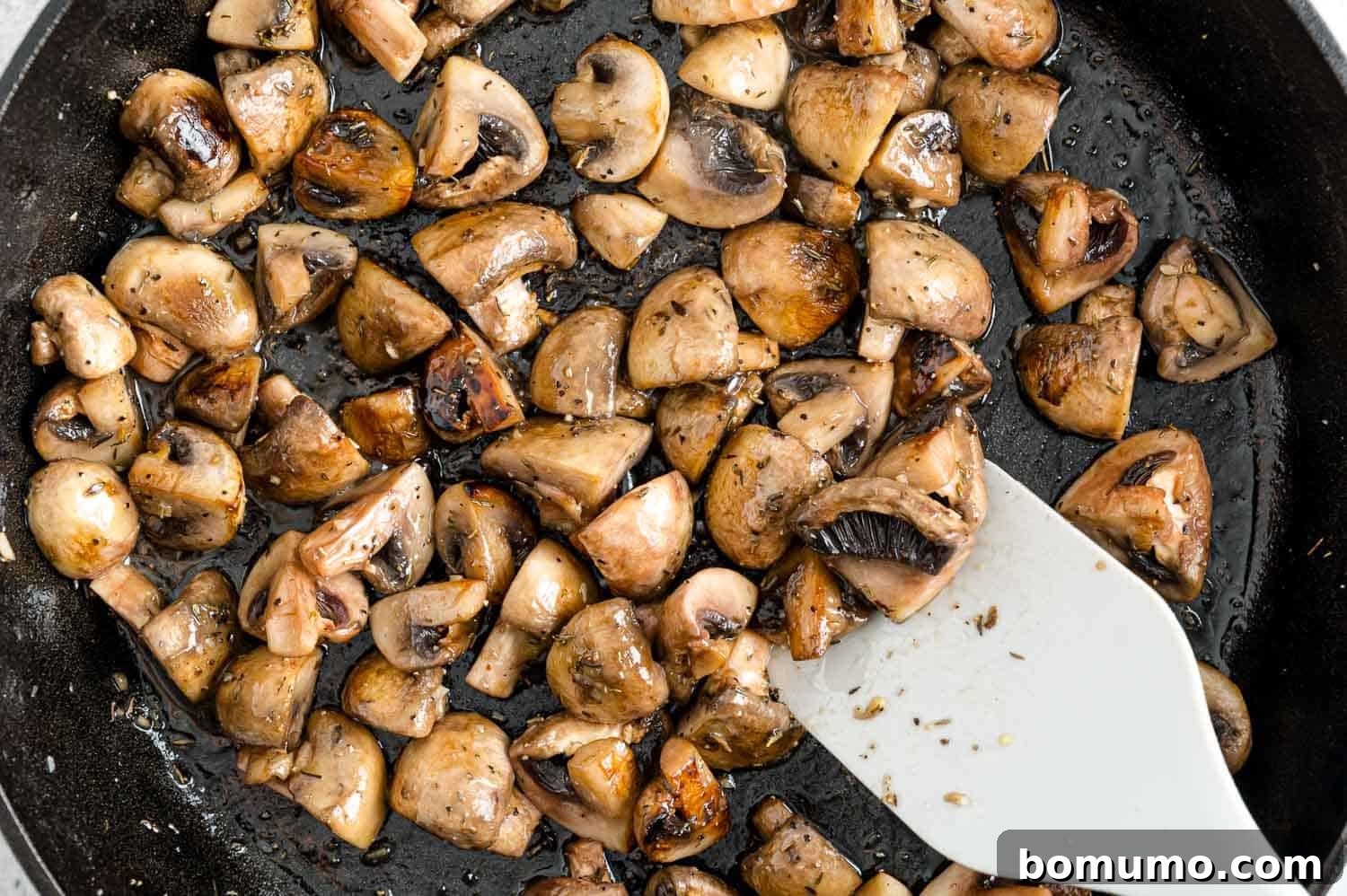 A close-up of beautifully cooked mushrooms simmering in a rich Marsala wine sauce in a frying pan, indicating the final stage of preparation.