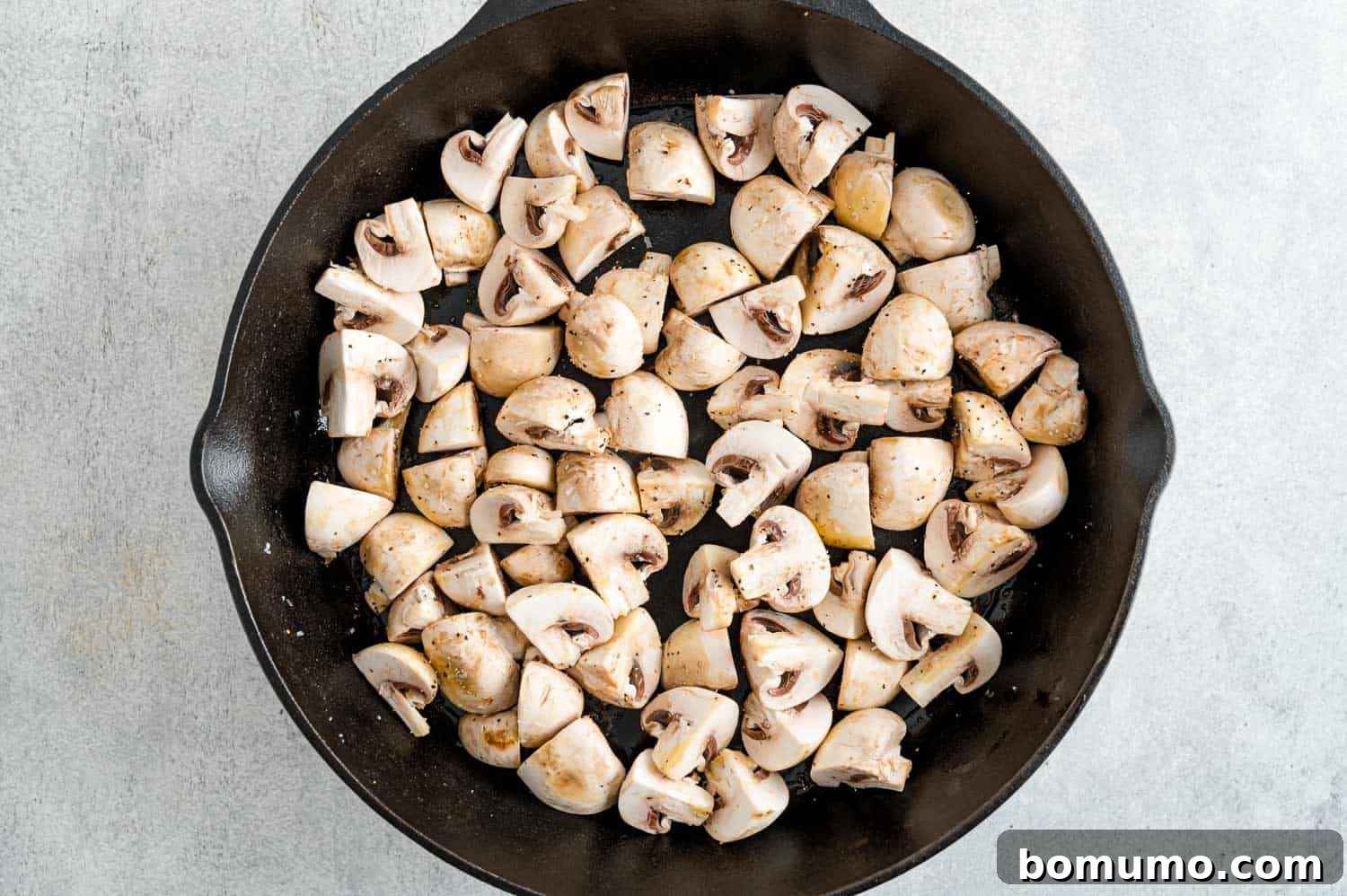 Raw, seasoned mushrooms neatly arranged in a single layer in a hot frying pan, poised for the initial sautéing phase.