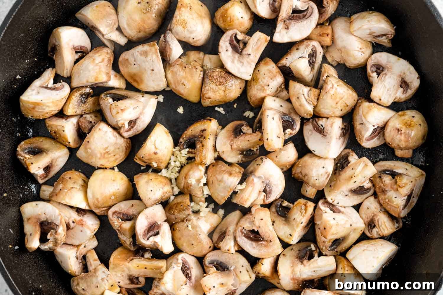 Freshly minced garlic being added to the sautéed mushrooms in the pan, initiating the aromatic infusion stage.