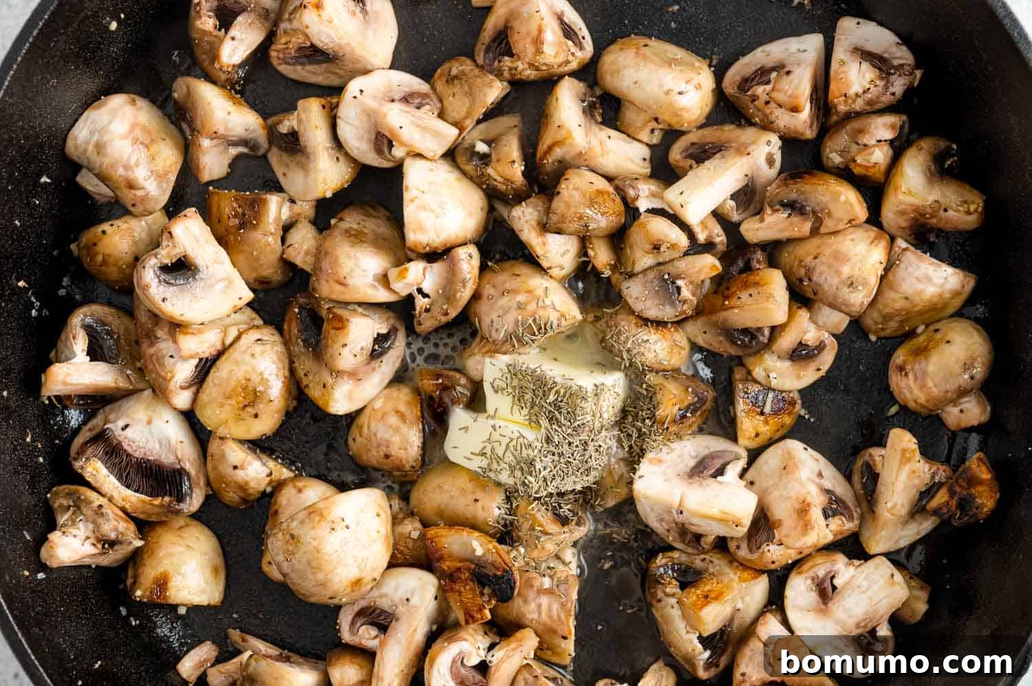 A pat of butter melting into the pan with mushrooms, enhancing the richness and flavor of the dish.