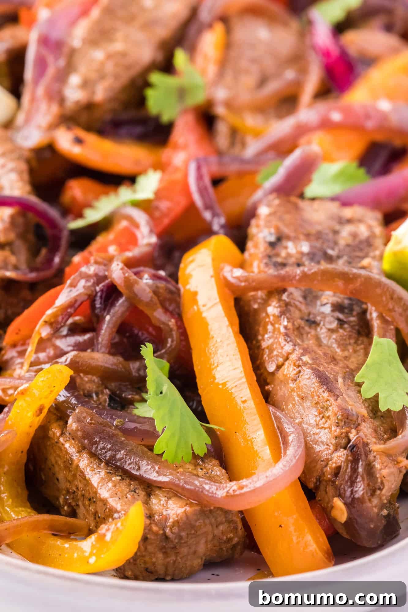 Close-up view of succulent steak fajitas generously garnished with fresh, vibrant cilantro, highlighting the perfectly cooked and marinated meat and vegetables, ready to be devoured.