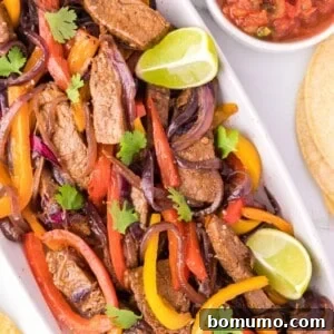 Overhead view of sizzling steak fajitas with colorful peppers and onions in a cast iron pan, ready for serving.