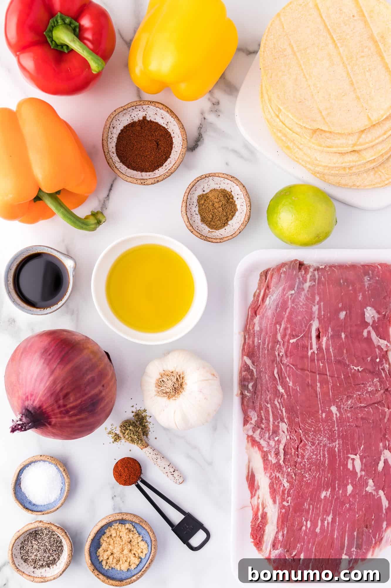 A vibrant and appealing selection of fresh, raw ingredients laid out on a clean surface, including neatly sliced flank steak, an assortment of colorful bell peppers, red and yellow onions, and fresh limes, all perfectly prepped for making delicious steak fajitas.