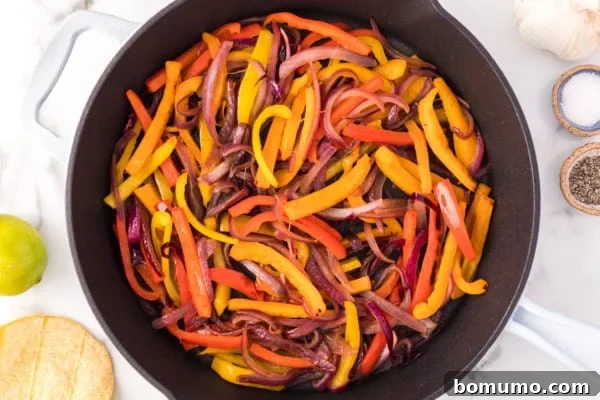 Overhead view of vibrant, thinly sliced bell peppers (red, yellow, green) and white onions sizzling and caramelizing in a large, hot cast-iron skillet on the stovetop, releasing their sweet aromas.