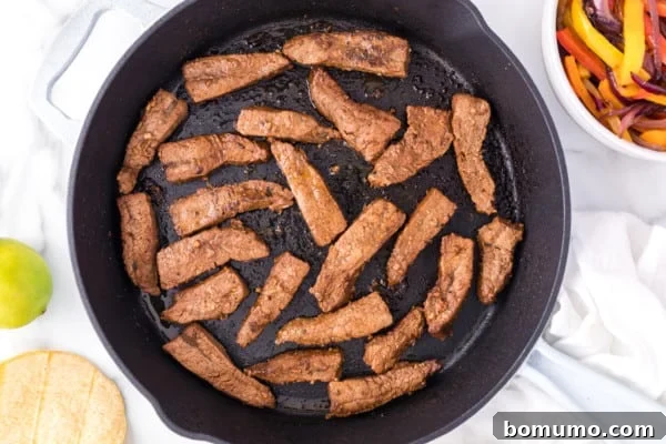 Overhead view of thinly sliced, marinated steak pieces sizzling and searing to a perfect brown in a hot skillet, cooked in small batches to achieve an ideal crust and juicy interior.