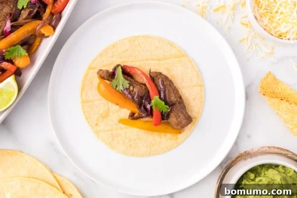 Overhead view of a soft, warm tortilla placed on a plate, generously topped with a heaping serving of sizzling steak fajita mixture, comprising tender beef, colorful peppers, and caramelized onions.