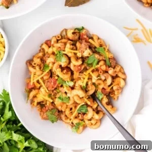Crockpot goulash in a white bowl with a spoon, ready to eat.