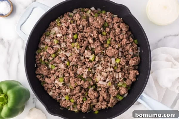 Overhead view of browned ground beef with diced onions and bell peppers in a skillet, ready for the slow cooker.