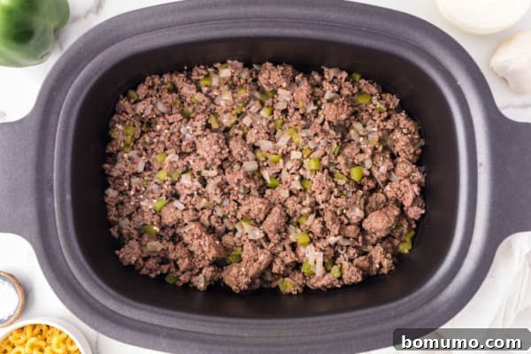 Overhead view of browned ground beef and cooked vegetables transferred to the bottom of a crockpot, forming the base of the goulash.