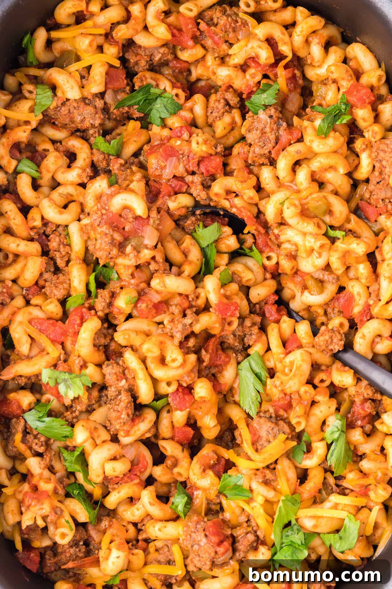 Overhead close up view of crockpot goulash garnished with fresh parsley in a white bowl, ready to be enjoyed.