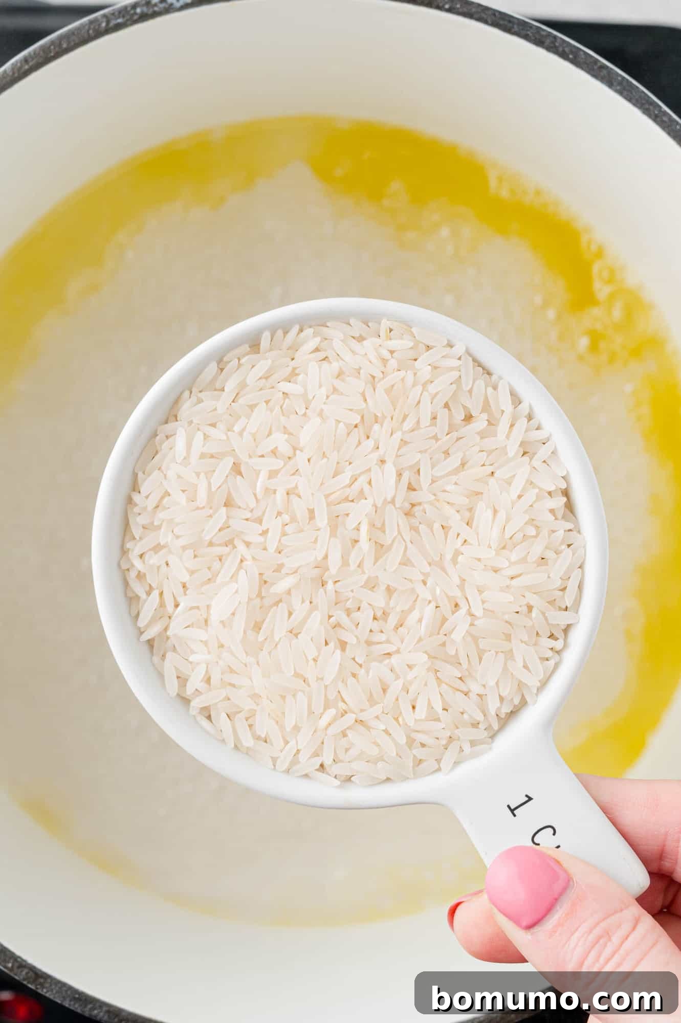 Jasmine rice being carefully poured from a measuring cup into a pan with boiling water.
