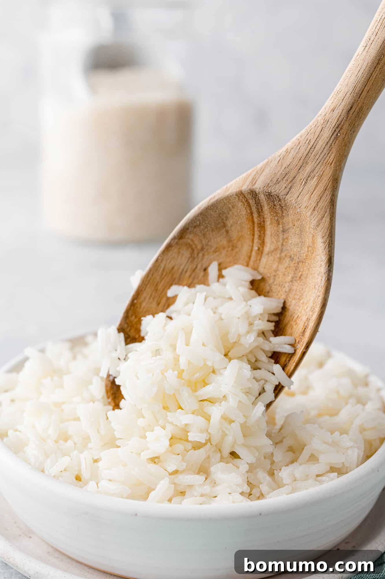 A wooden spoon scooping fluffy jasmine rice into a pristine white bowl.