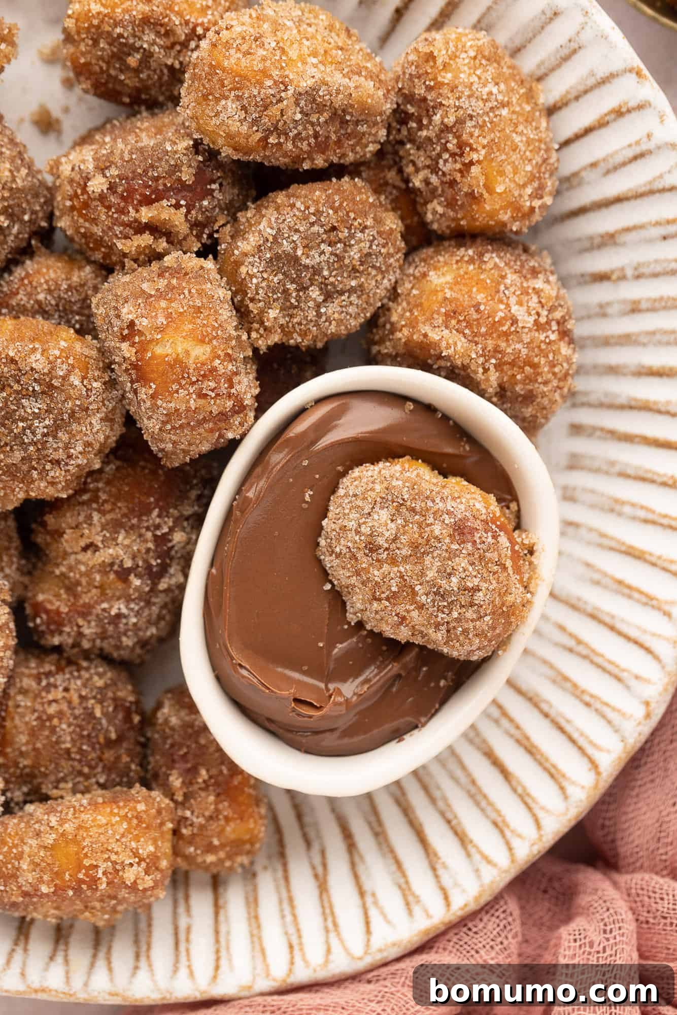 Close up overhead view of a cinnamon sugar pretzel bite resting in a small bowl of nutella, nestled in a larger bowl of pretzel bites.