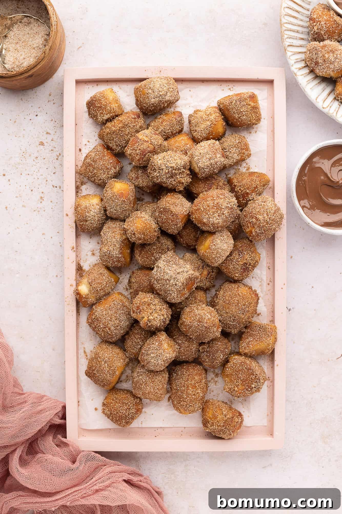 Overhead view of cinnamon sugar pretzel bites on a rectangular platter, next to a bowl of nutella for dipping.