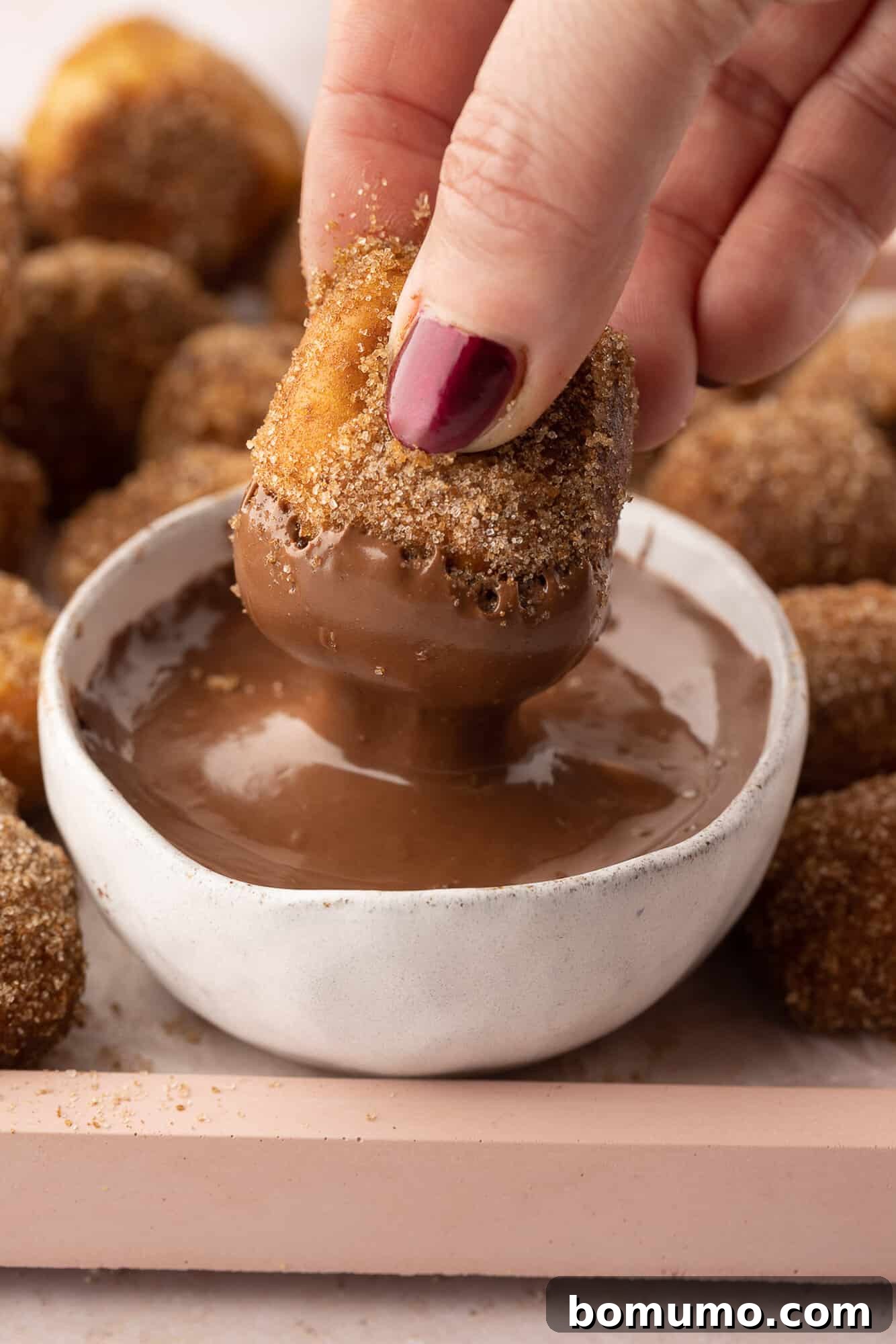 A hand dipping a cinnamon sugar pretzel bite into a bowl of nutella.