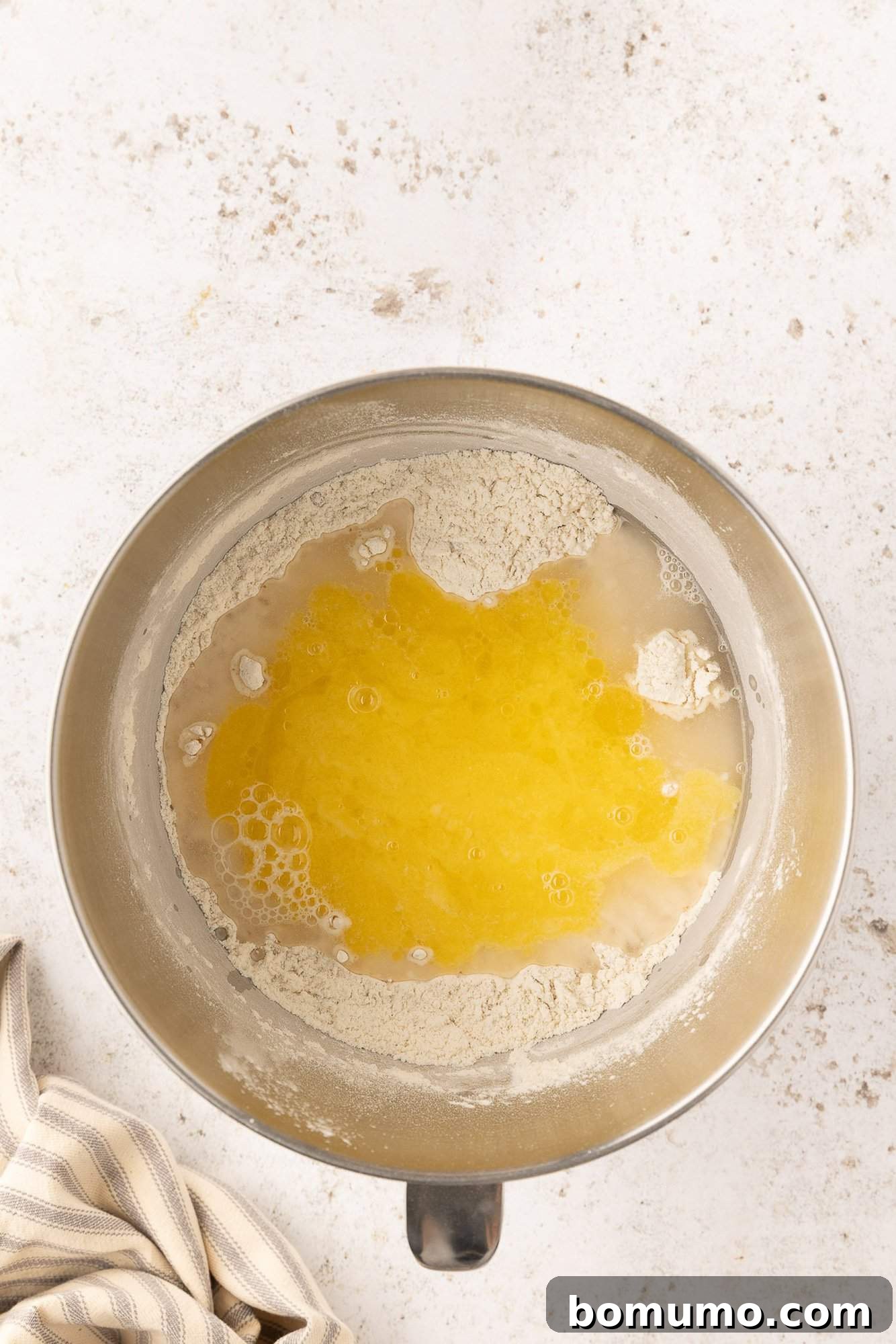 Warm water and melted butter added to dry ingredients in a metal bowl.