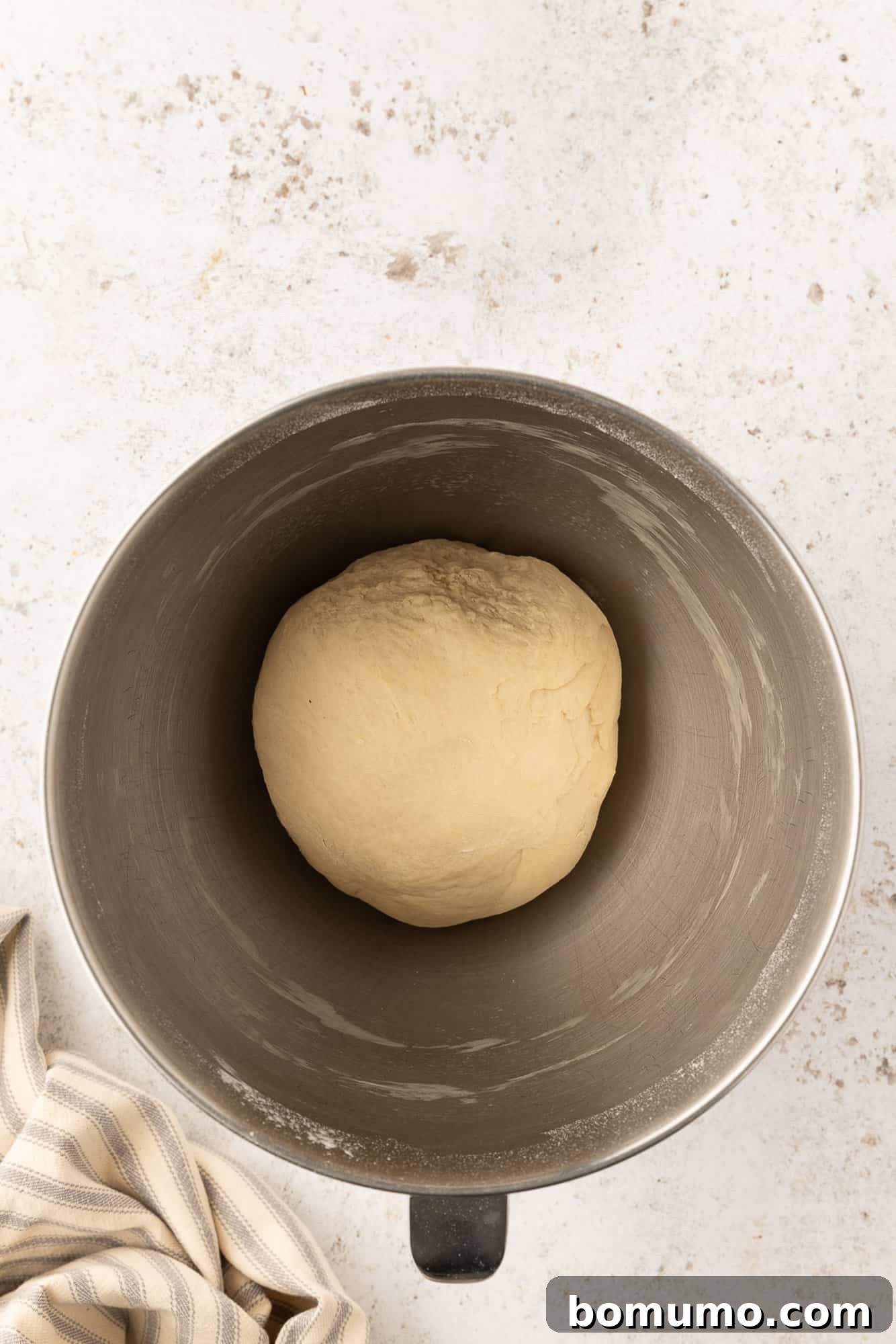A round pretzel dough ball in a metal mixing bowl.