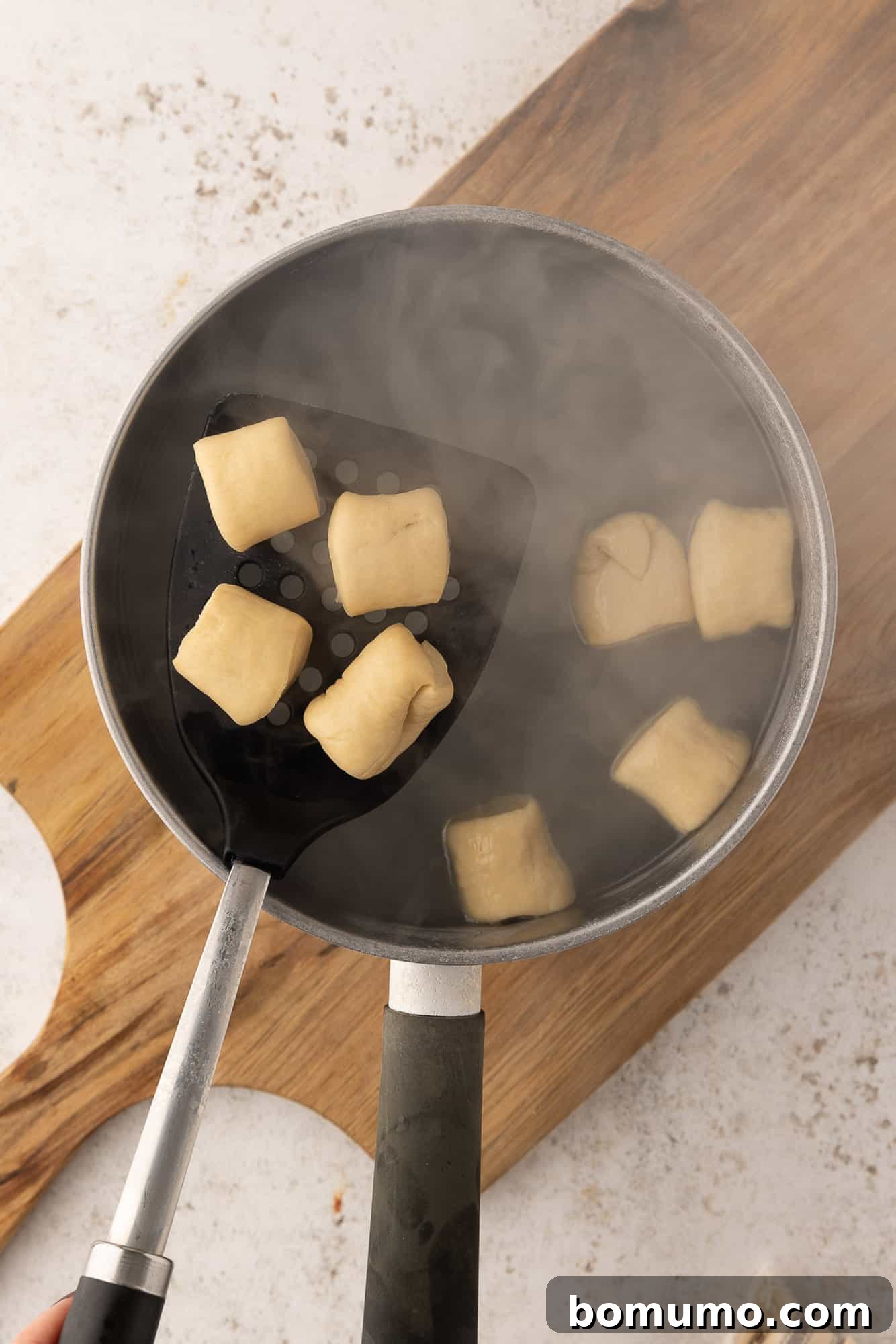 A slotted spoon removing boiled pretzel bites from a baking soda bath.