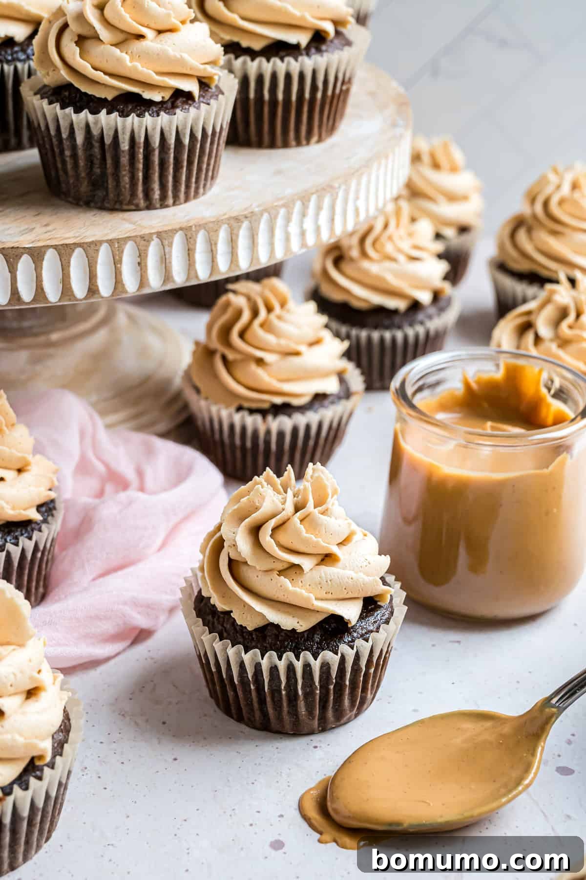Peanut butter frosting elegantly piped on multiple chocolate cupcakes, with some artfully arranged on a tiered cake stand.