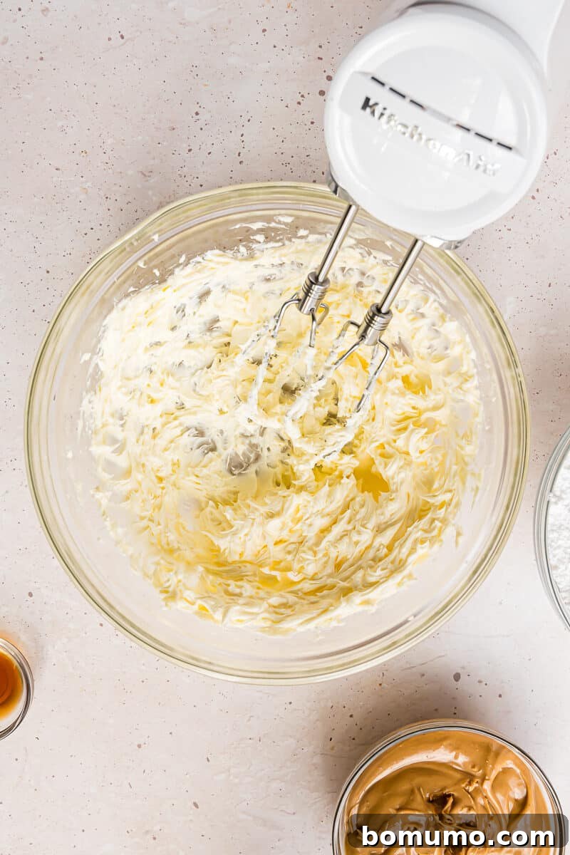Softened unsalted butter being vigorously beaten with an electric mixer in a large bowl, achieving a light and airy consistency.