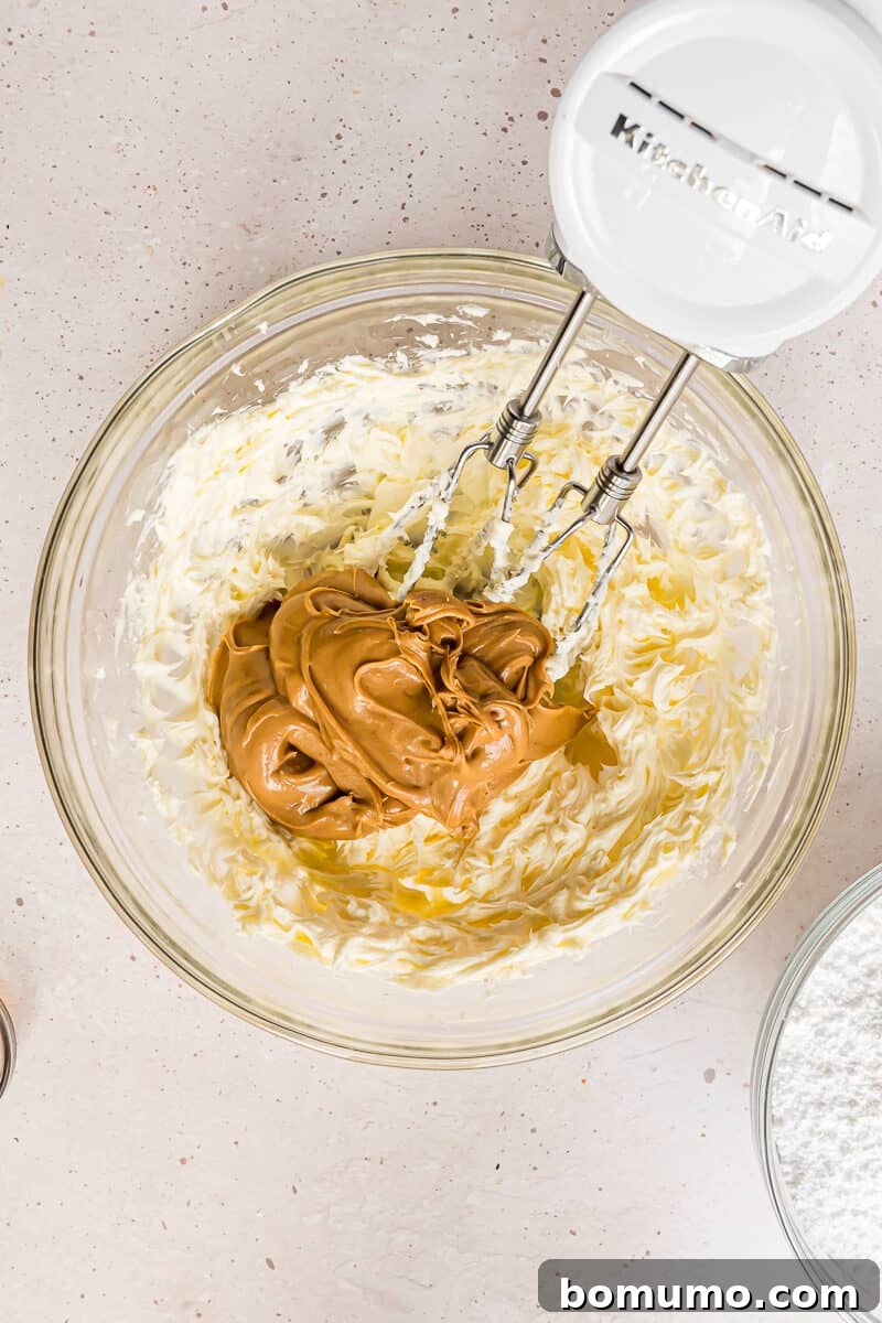 Rich creamy peanut butter being carefully added to the bowl of already beaten, fluffy butter.