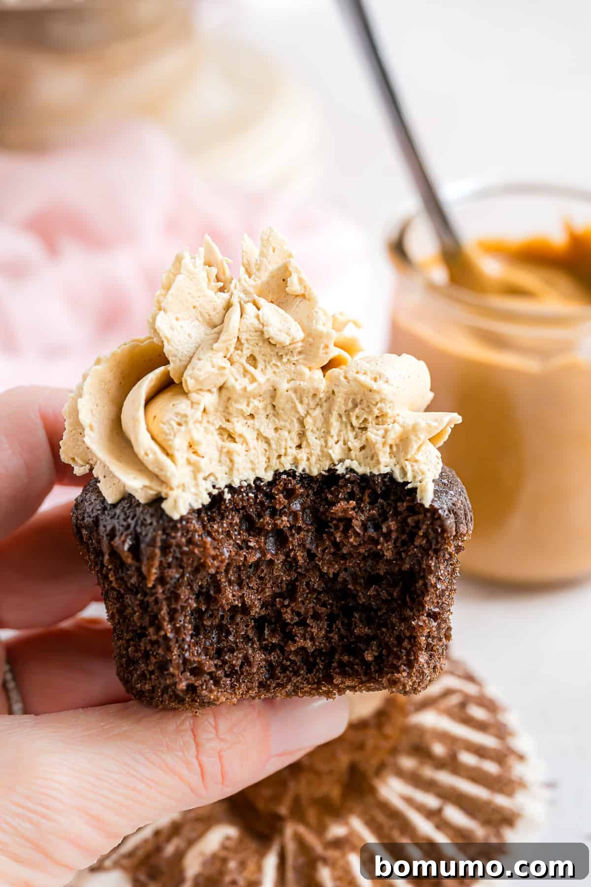 A rich chocolate cupcake generously topped with piped peanut butter frosting, with a delectable bite removed, showcasing its creamy texture.