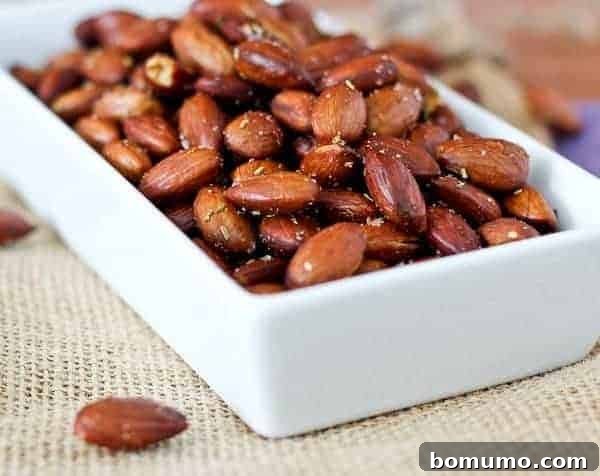 A close-up of crunchy olive oil and rosemary roasted almonds in a serving dish, highlighting their golden brown texture.