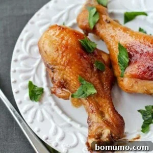 Two drumsticks on white plate garnished with fresh chopped parsley leaves.