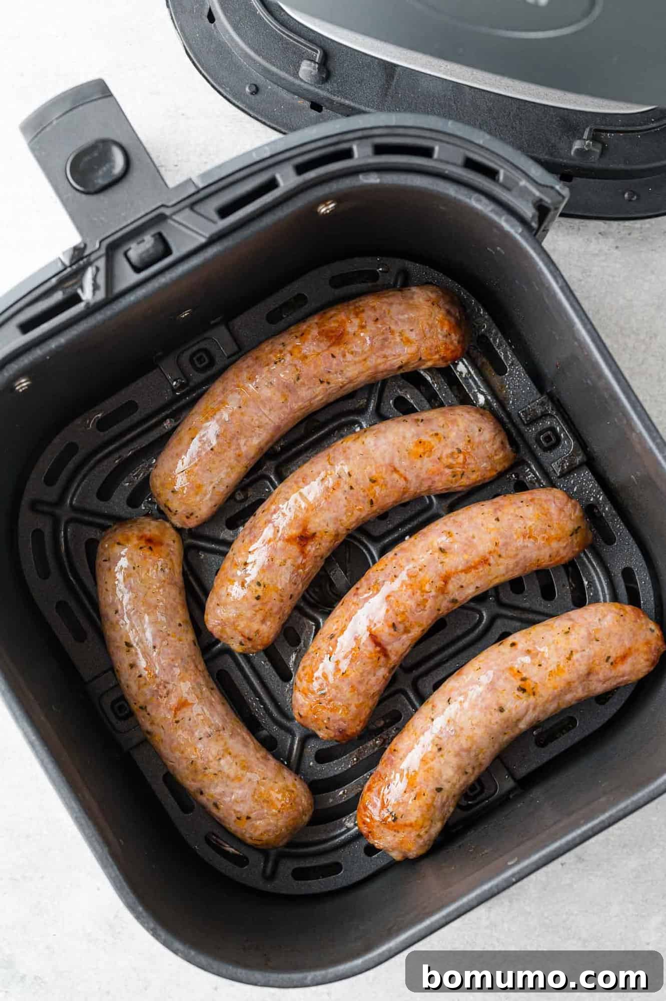 Overhead view of cooked Italian sausage in air fryer basket.