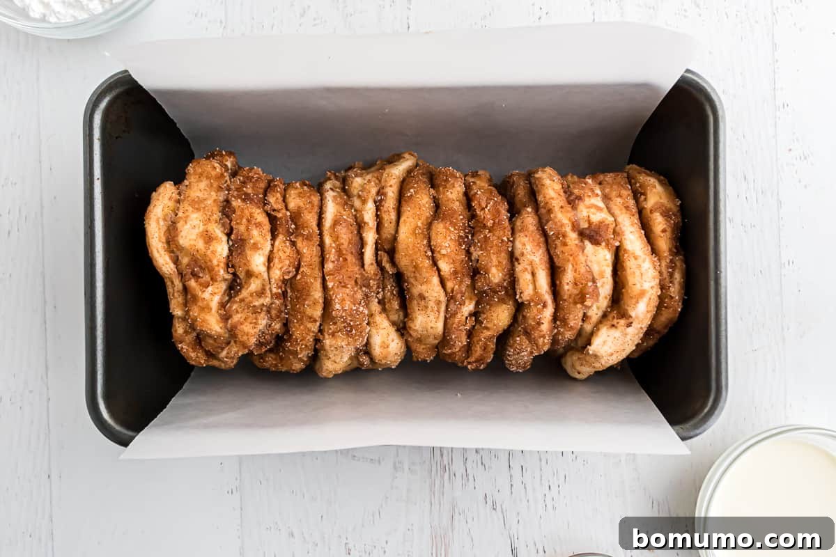 Cinnamon sugar coated biscuit pieces in parchment paper lined loaf pan.