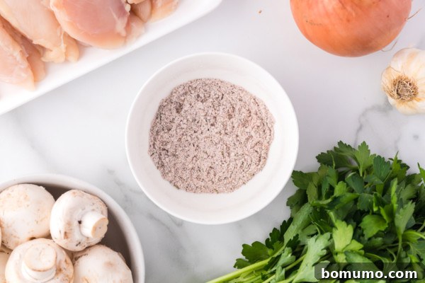 Overhead view of chicken seasoning in a bowl next to a bunch of parsley, a bowl of mushrooms, and a plate of uncooked chicken.