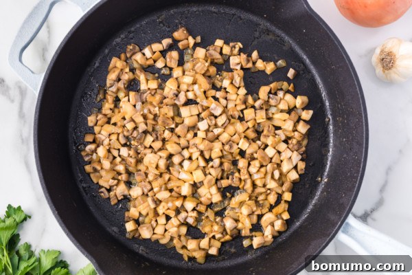 Finely diced mushrooms and onions gently sauteeing in a skillet, forming the flavorful base for the creamy sauce.