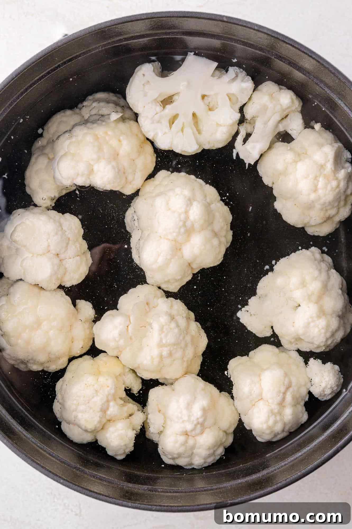 Cauliflower florets in a large black pot.