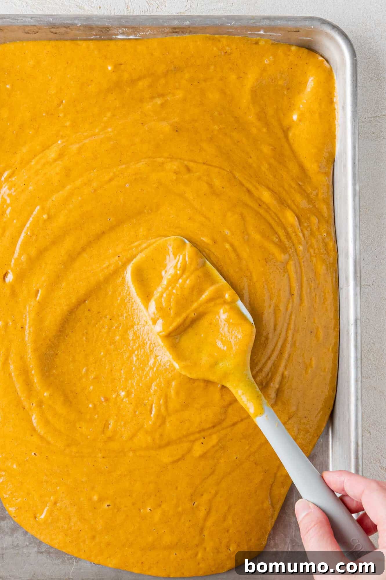 Autumn Pumpkin Spice Bars 12 Smooth, orange pumpkin batter being meticulously spread into a prepared sheet pan, creating an even layer ready for baking.