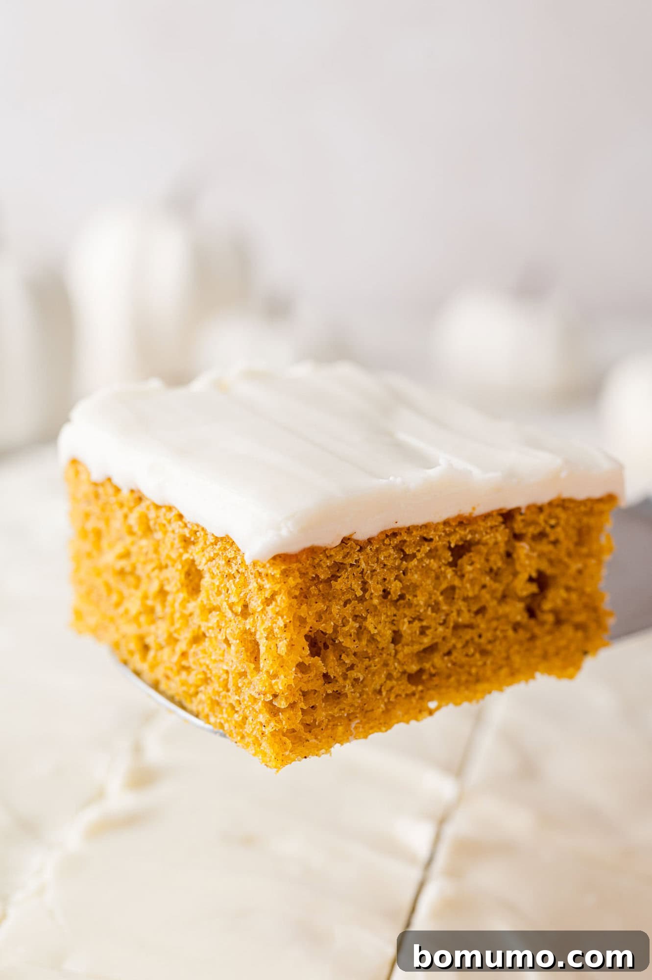 Autumn Pumpkin Spice Bars 17 A perfectly frosted pumpkin bar being carefully lifted out of the pan with a spatula, revealing its tender cake and thick layer of cream cheese frosting.