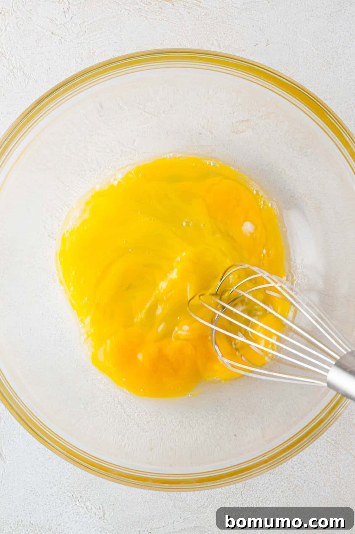 Autumn Pumpkin Spice Bars 5 A whisk gracefully beating fresh eggs in a clear mixing bowl, preparing them for the next stage of combining wet ingredients.
