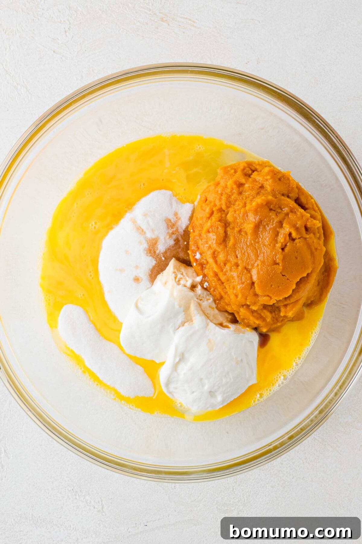 Autumn Pumpkin Spice Bars 6 A collection of vibrant wet ingredients, including pumpkin purée, Greek yogurt, and vanilla, beautifully arranged in a clear glass bowl before being fully mixed.