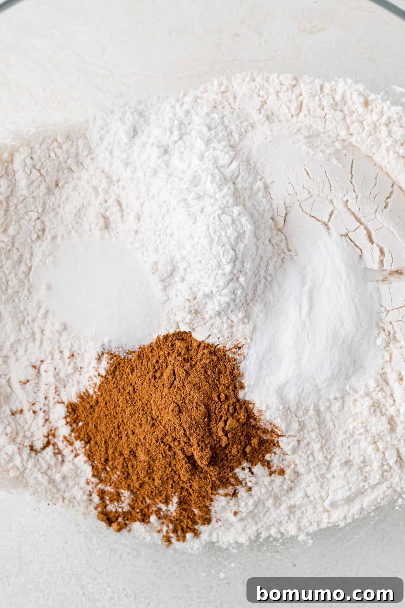 Autumn Pumpkin Spice Bars 8 All the dry ingredients for the pumpkin bars, including flour, pumpkin pie spice, baking powder, baking soda, and salt, carefully measured and placed in a clear glass mixing bowl, uncombined.