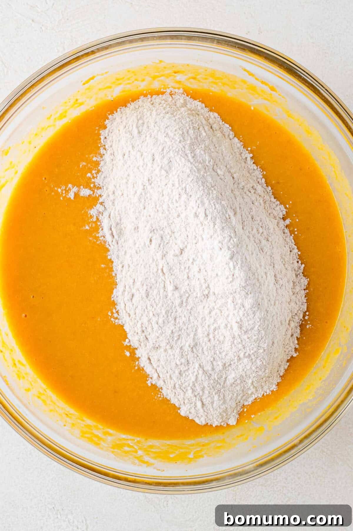Autumn Pumpkin Spice Bars 10 The dry ingredient mixture delicately added on top of the smooth, vibrant wet pumpkin batter in a large mixing bowl, poised for gentle incorporation.